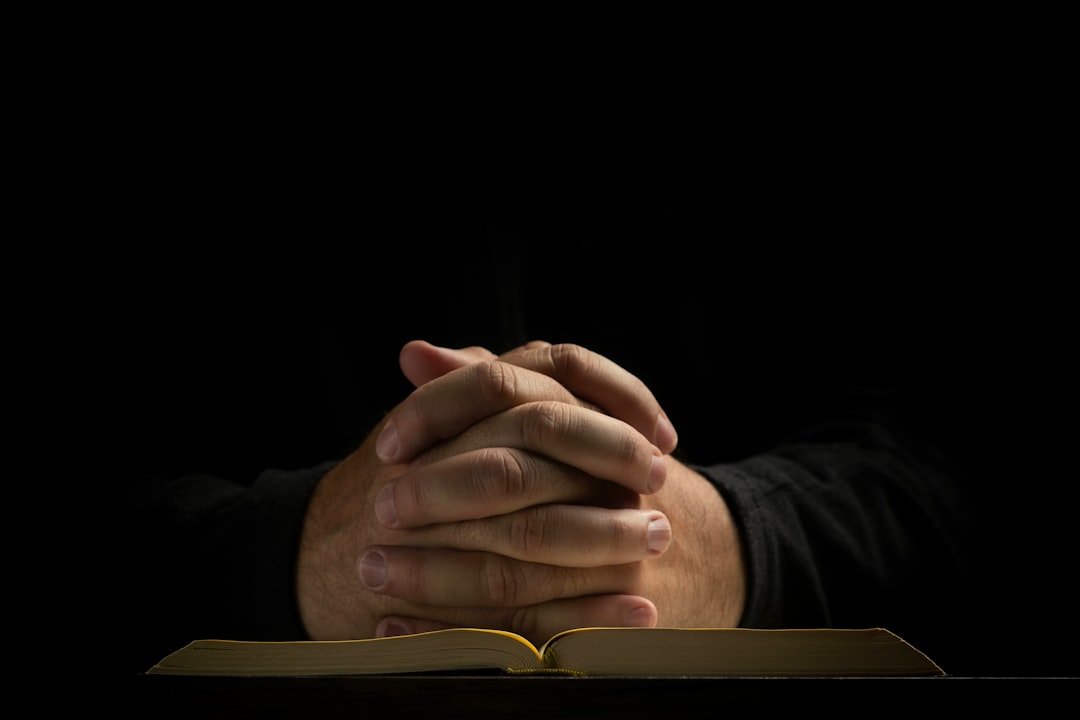 Hands folded on a book in prayer, warm light